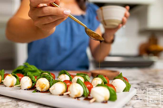 spoon drizzling balsamic reduction over caprese skewers