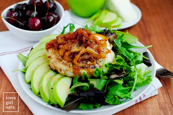 a turkey burger on a salad with sliced apples and caramelized onions