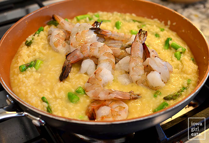 shrimp being added to a skillet of shrimp and asparagus risotto