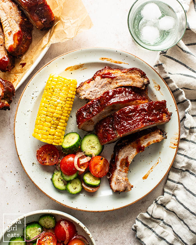 baked ribs on a plate with salad and corn