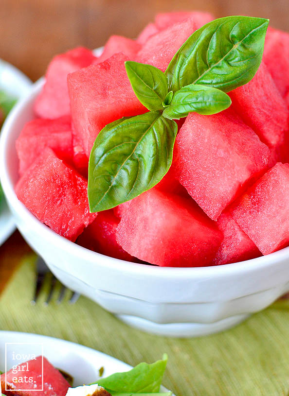 fresh cut watermelon in a bowl with a sprig of fresh basil