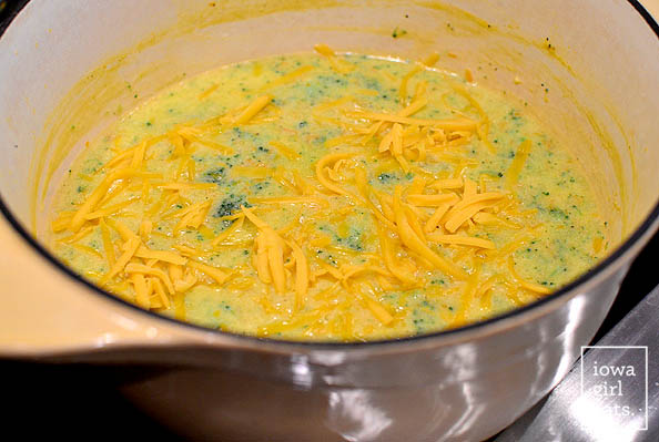 shredded cheddar cheese being melted into a pot of broccoli cheese soup