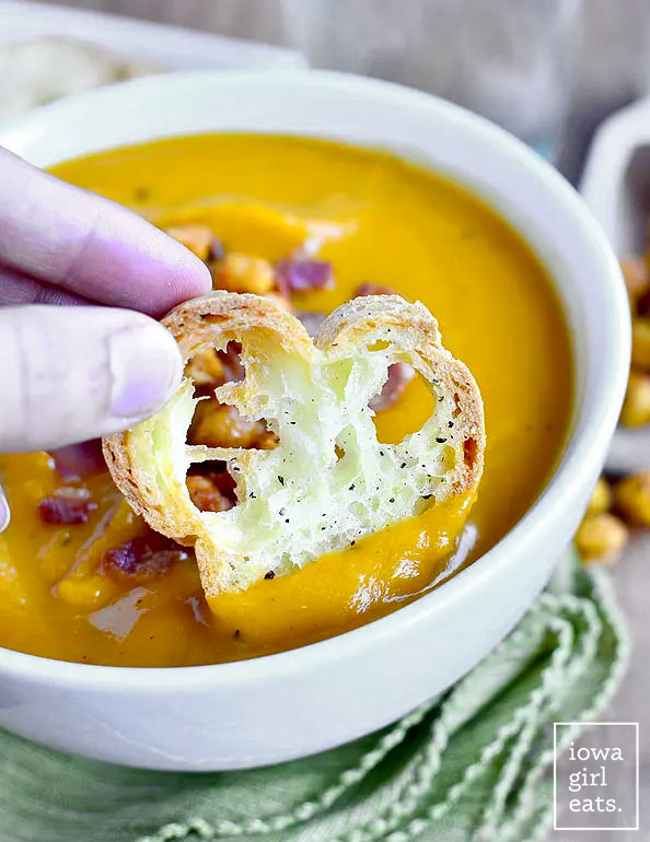 hand dunking a crostini into butternut squash soup