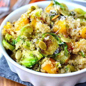 quinoa with caramelized butternut squash and roasted brussels sprouts in a dish topped with pepitas