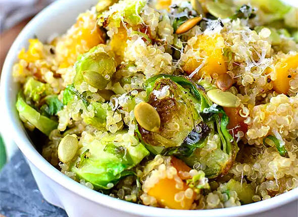 quinoa with caramelized butternut squash and roasted brussels sprouts in a dish topped with pepitas