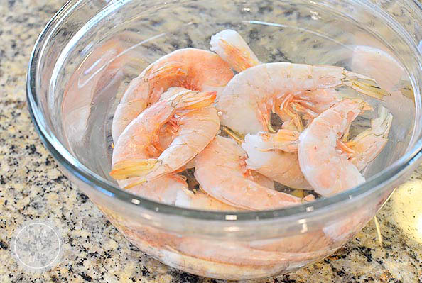 raw shrimp thawing in a bowl of water