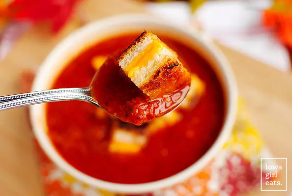 spoon scooping up roasted tomato soup with a grilled cheese crouton on top