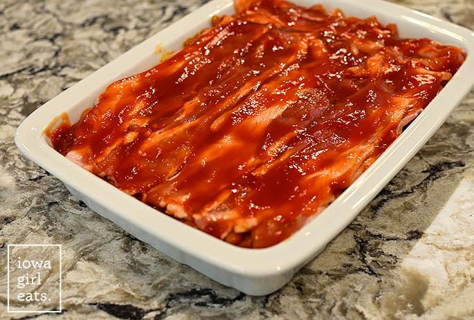 bacon slices placed on top of a baking pan of baked beans