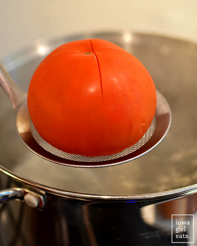 cucharón sosteniendo un tomate sobre una olla de agua hirviendo