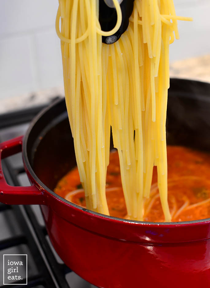 adding cooked spaghetti to a pot of pomodoro sauce