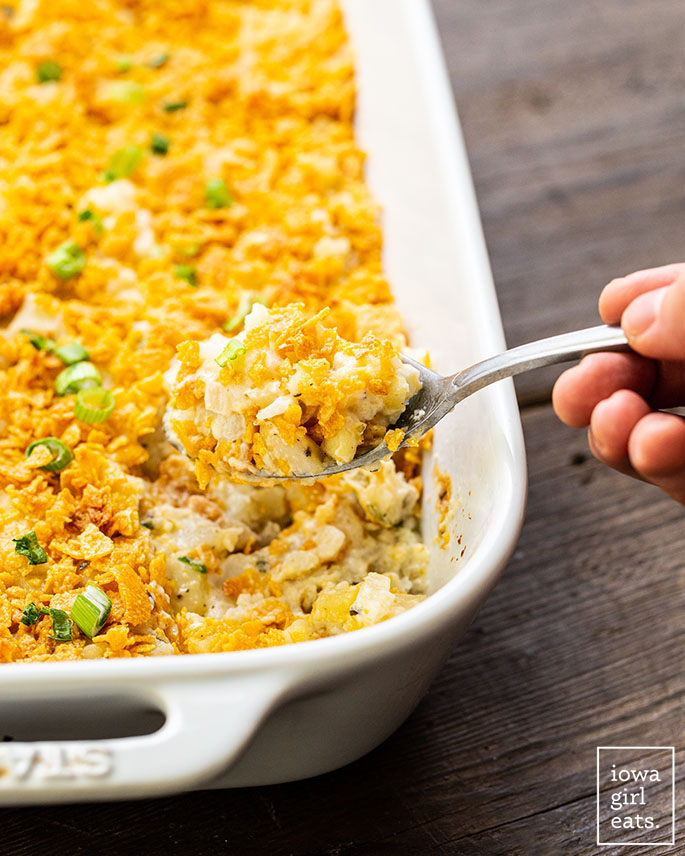 hand scooping gluten free cheesy potatoes from a casserole dish