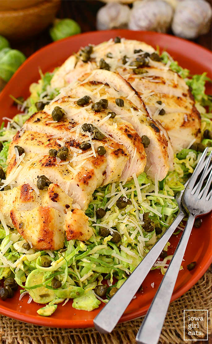 a platter of shredded brussels sprout caesar salad with sliced chicken
