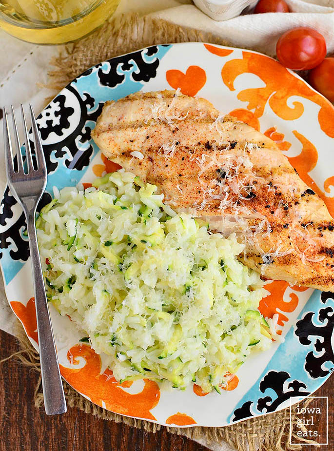 overhead photo of a scoop of creamy cheesy zucchini rice on a plate with grilled chicken