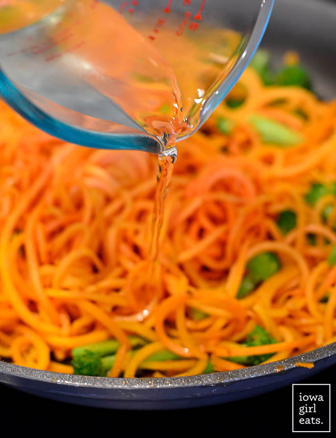 water being drizzled into a hot skillet with sweet potato noodles
