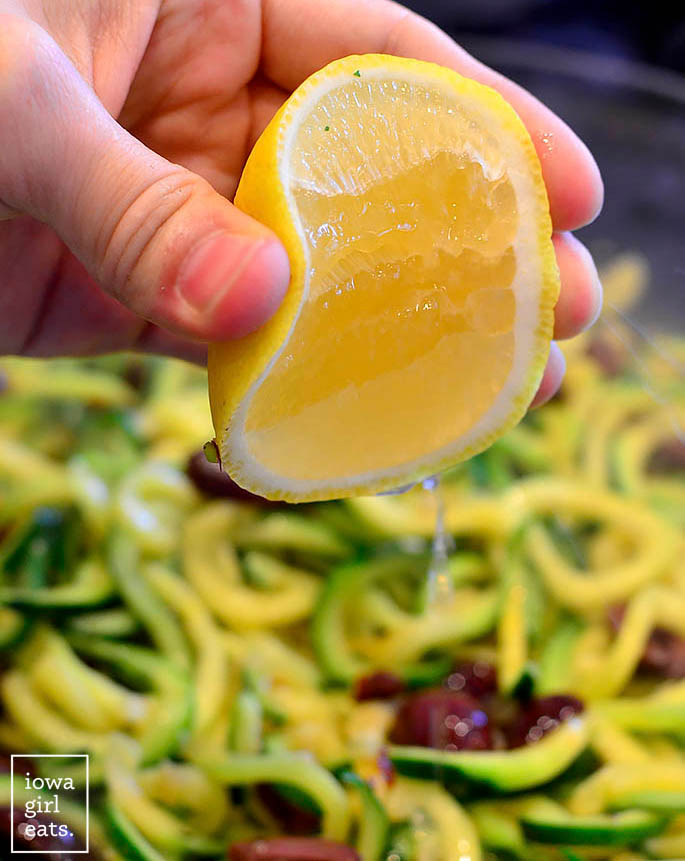 fresh lemon juice being squeezed into a skillet of zoodles