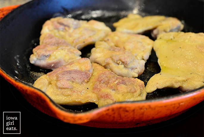 dredged chicken thighs sauting in a skillet