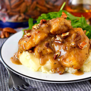 saucey chicken thighs over cooked mashed potatoes on a plate