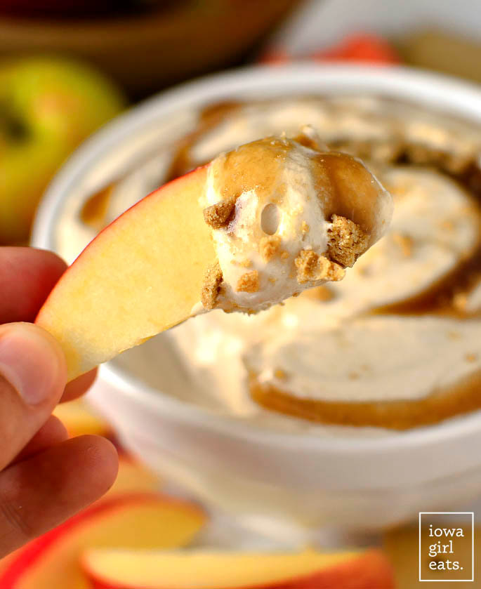 apple slice dipping in to a bowl of caramel apple cheesecake dip