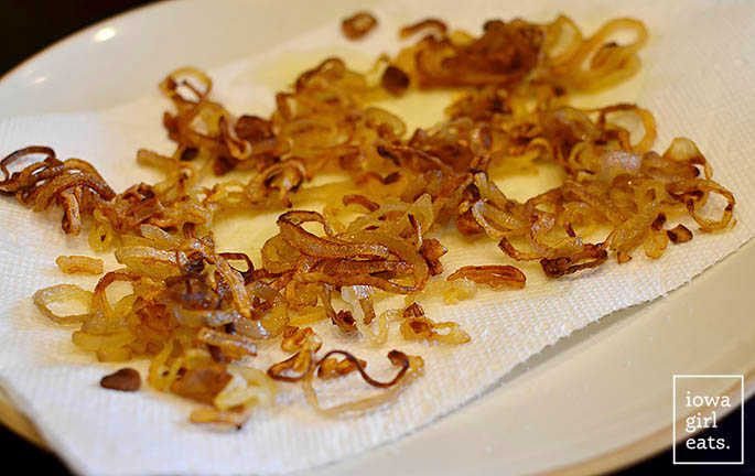 homemade crispy shallot rings draining on a paper towel lined plate