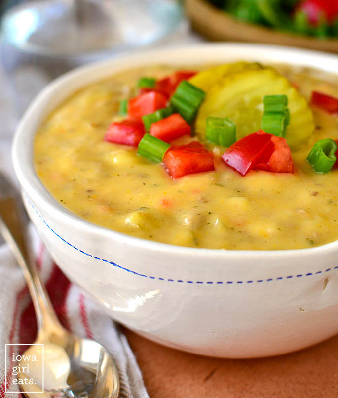 healthy cheeseburger soup with pickles and tomatoes on top
