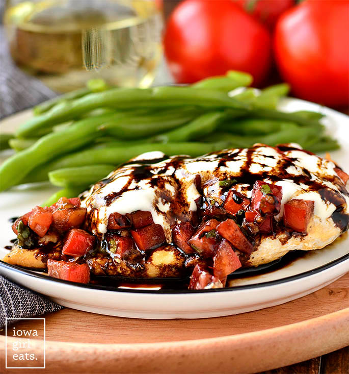 Photo of Mozzarella Bruschetta Chicken and green beans on a plate with a glass of wine.