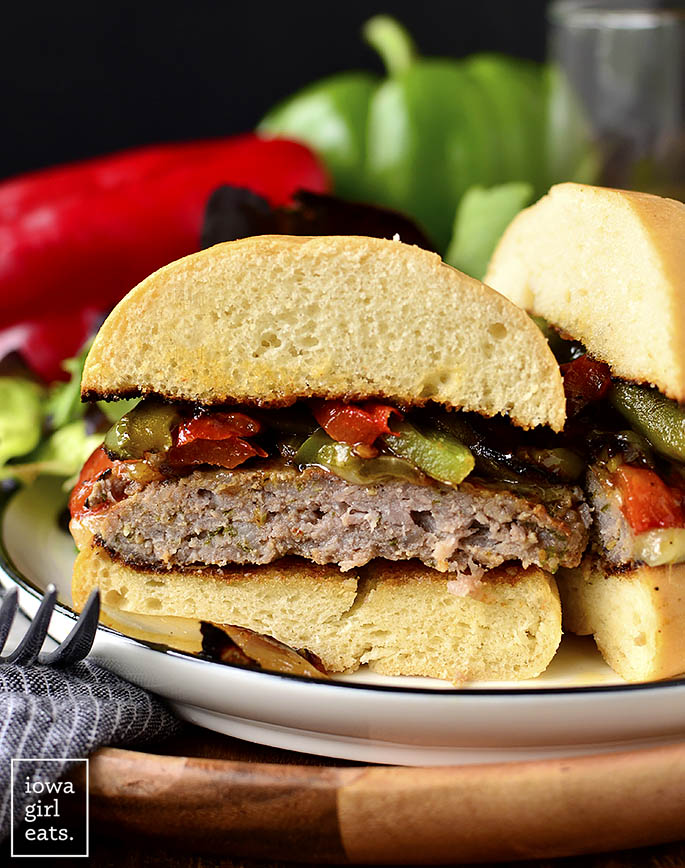 Italian Sausage and Peppers Cheeseburger sliced in half on a plate.