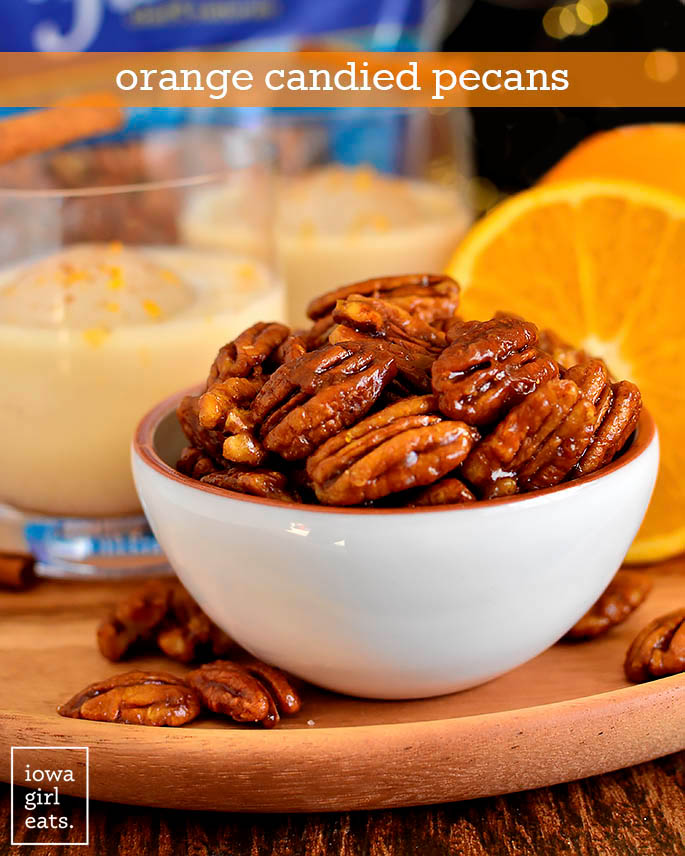 Bowl of Orange Candied Pecans with Spiked Eggnog glasses in the background