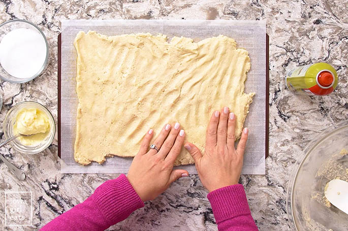 hands spreading gluten free cinnamon roll dough into a rectangle