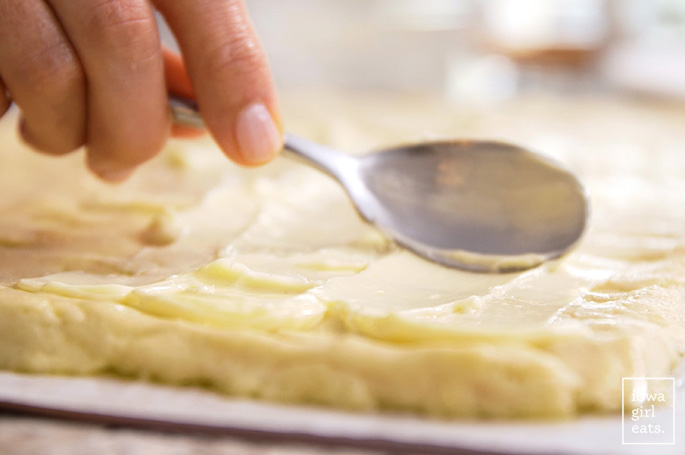 spoon spreading butter onto gluten free cinnamon roll dough