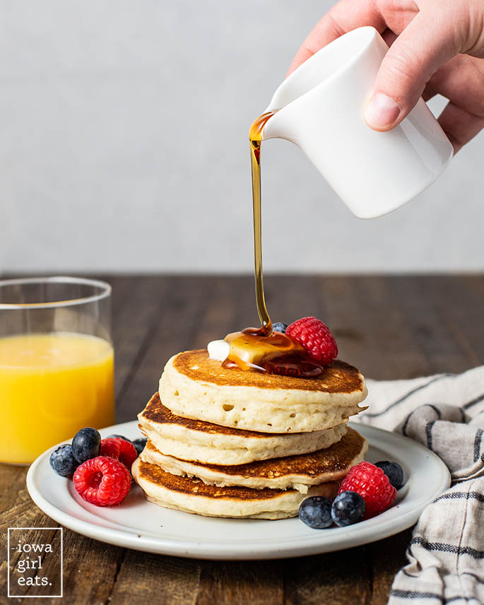 maple syrup being drizzled onto a stack of gluten free pancakes