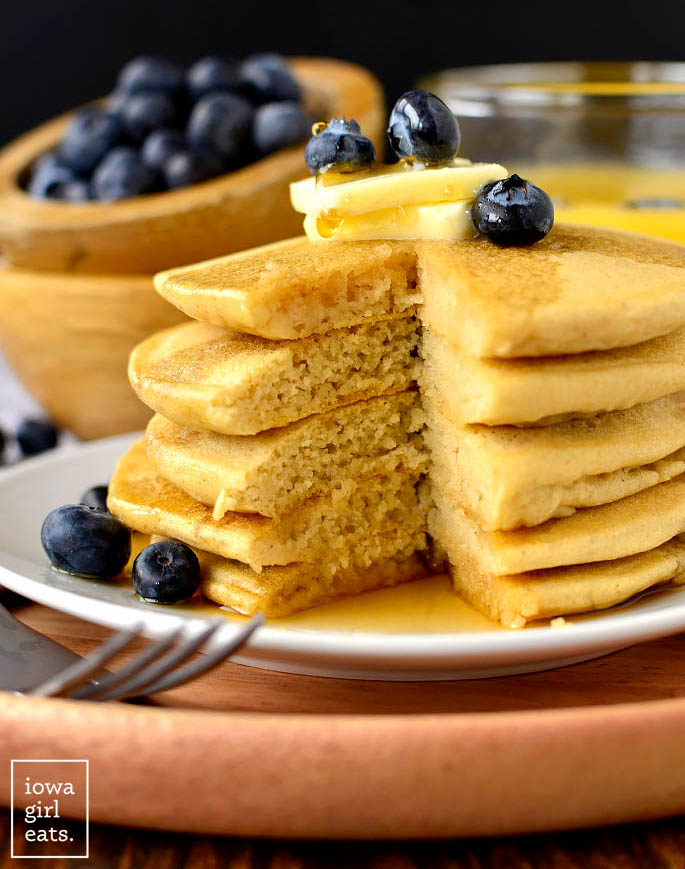 Gluten free pancakes stacked on plate with butter, maple syrup, and blueberries