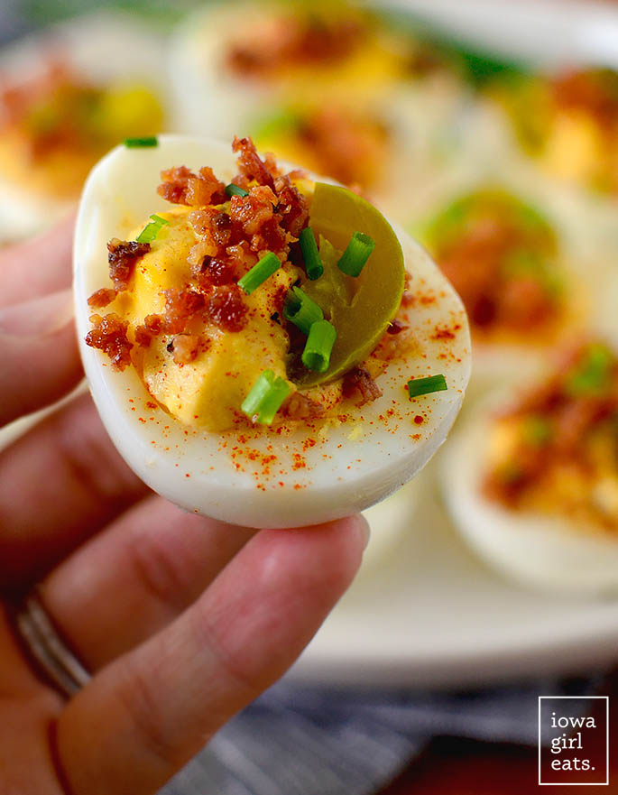 hand holding a deviled egg with bacon