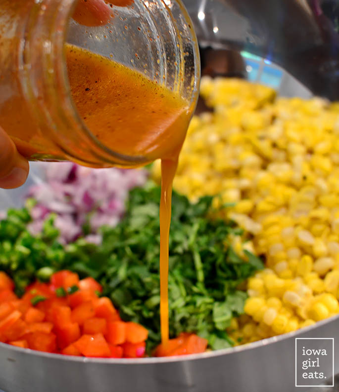 a jar of chili lime dressing being poured over southwest corn salad