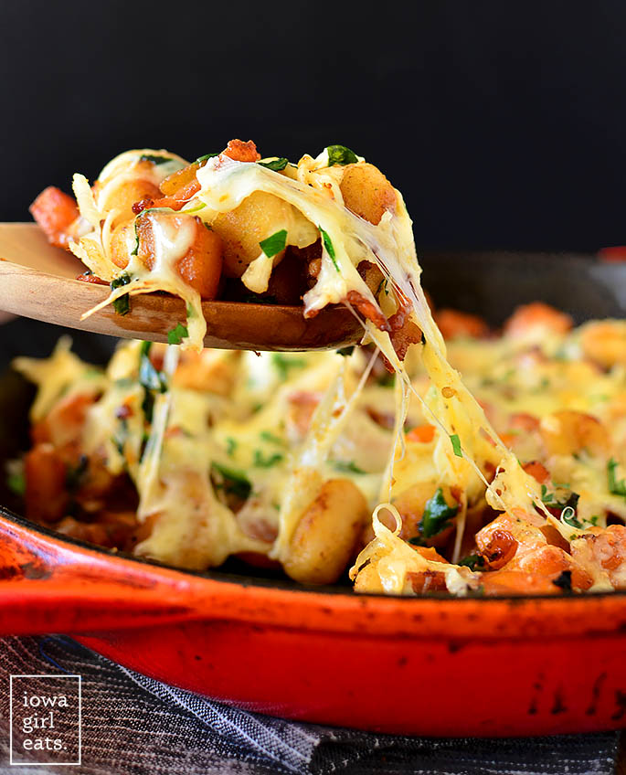 wooden spoon taking a scoop of Cheesy Bacon Butternut Squash Gnocchi out of a skillet