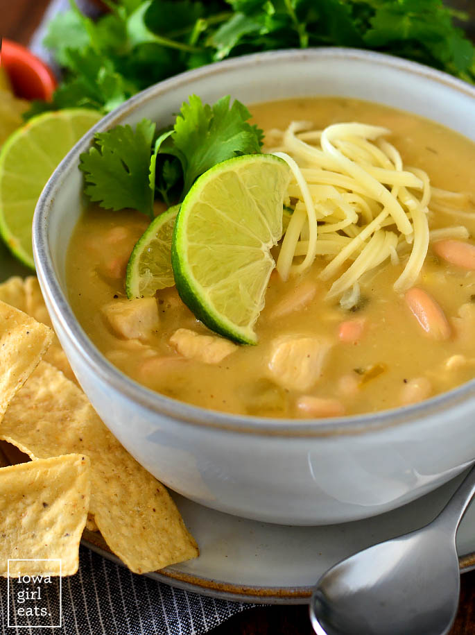 bowl of green chicken enchilada soup with shredded cheese and lime wedges
