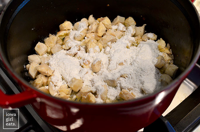 flour sprinkled over chicken breasts cooking in a soup pot