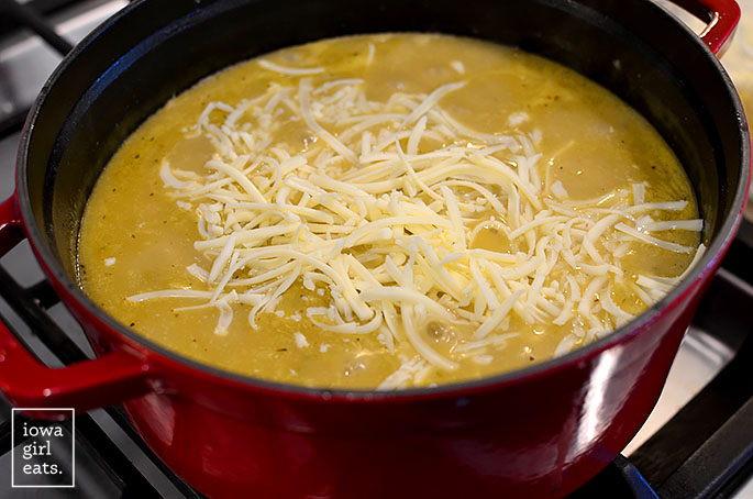 shredded cheese being stirred into a pot of green chicken enchilada soup