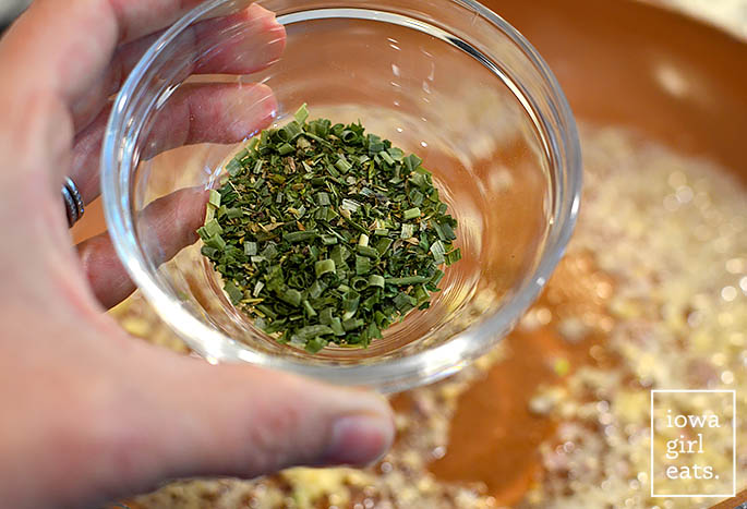 dried herbs being added to a skillet with pasta
