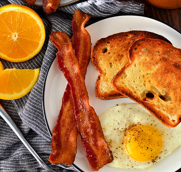 oven baked bacon slices on a plate with an egg and toast