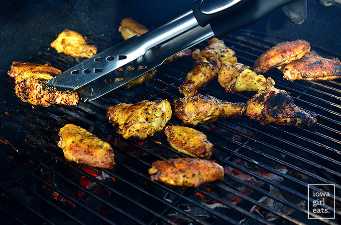 tongs turning chicken wings on the grill