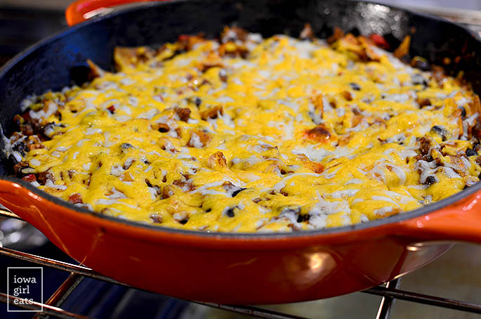 melted cheese on top of a skillet of beef and vegetable enchiladas