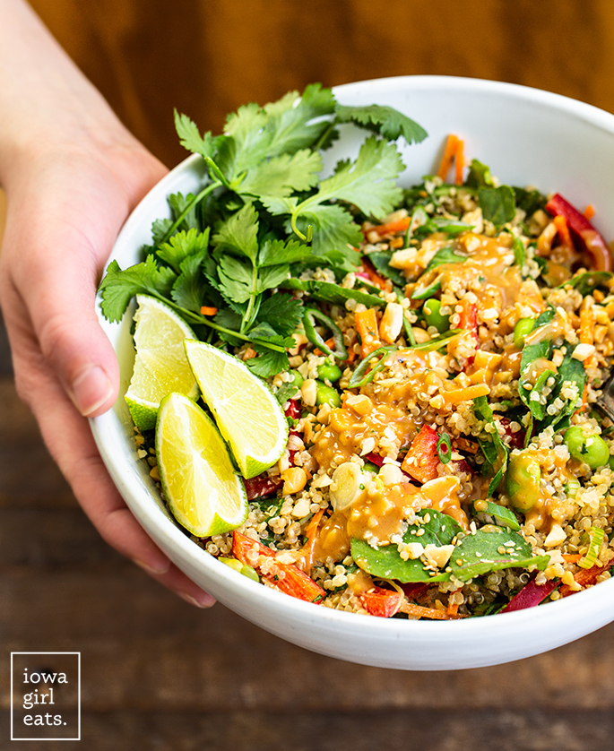 hands holding a bowl of thai quinoa salad with peanut dressing