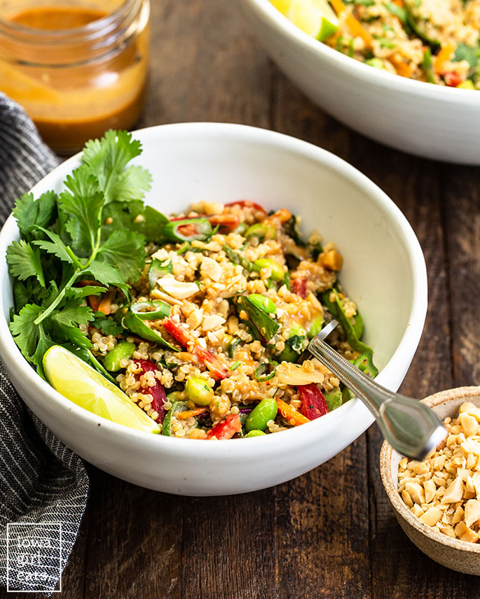 a fork in a bowl of thai quinoa salad with fresh herbs and lime wedges