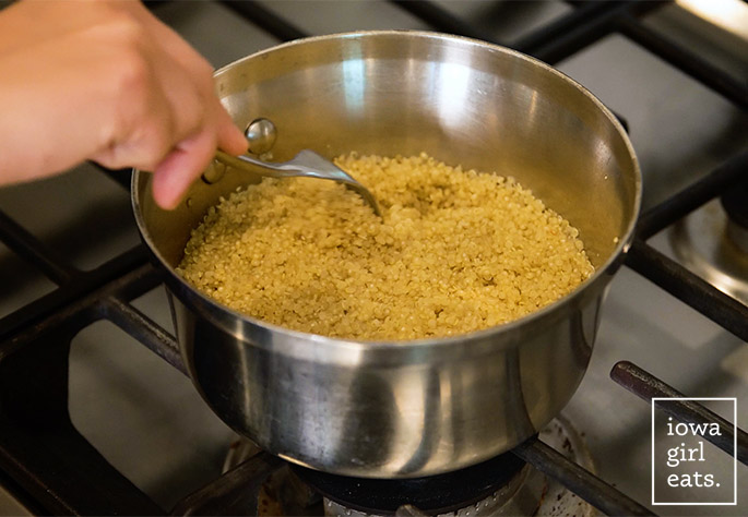 a hand fluffing a pan of cooked quinoa