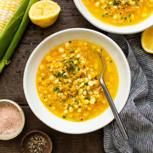 bowl of sweet corn soup with fresh herbs and a spoon insde