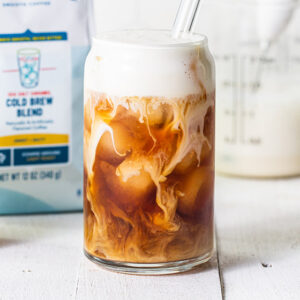 caramel cold foam being poured into a glass of iced coffee