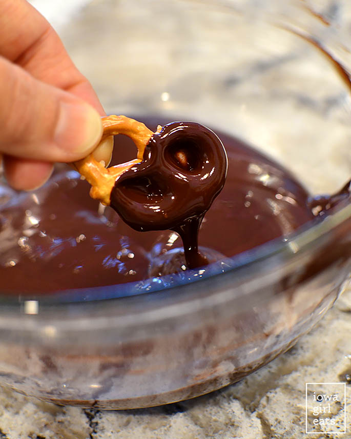 hand dipping pretzel into melted chocolate