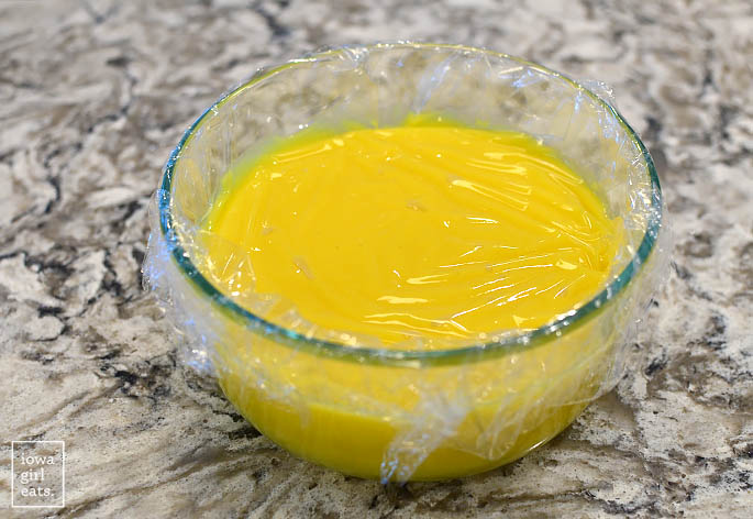 homemade lemon curd in a bowl with saran wrap on top