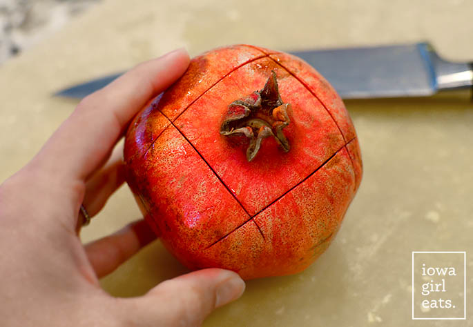 a scored pomegranate on a cutting board